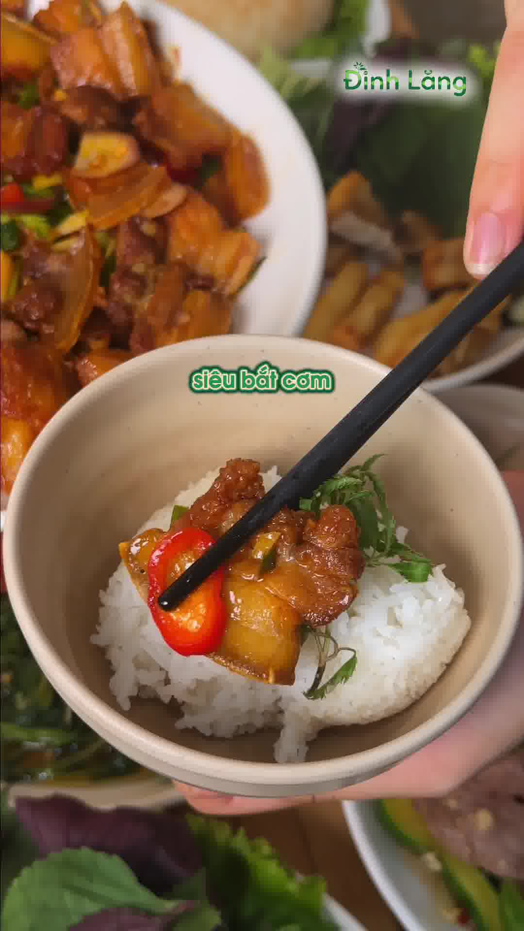 Miếng thịt ba rọi kho cháy cạnh óng ả kẹp cọng lá đinh lăng trên chén cơm niêu